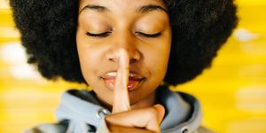 portrait of a pretty young afro girl showing silence gesture