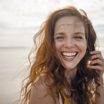 portrait of a redheaded woman, laughing happily on the beach