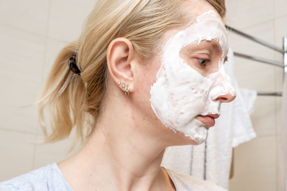 a portrait of a sad woman with problem acne skin making a cleansing purifying white facial mask, anti black spot and acne treatment