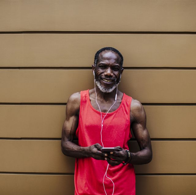 portrait of a senior african american man in red sportwear listening to music on his mobile phone while resting from his morning run