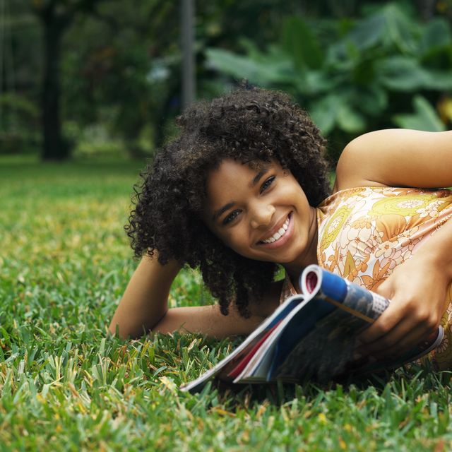 portrait of a young girl lying on a lawn reading a magazine