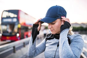 a portrait of a young sporty woman putting a cap on her head outside in a city