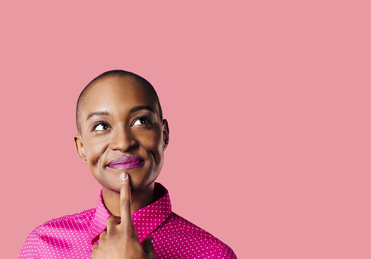 portrait of a young woman in pink shirt with finger on mouth looking up thinking, isolated on pink studio background
