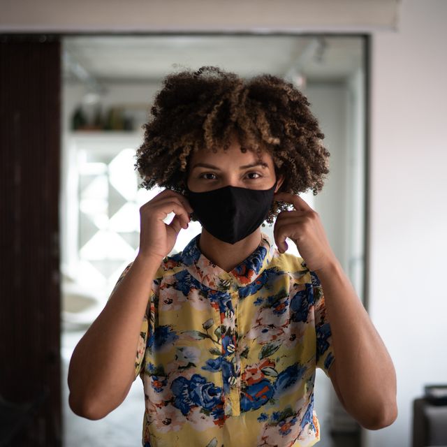 portrait of a young woman putting on protective face mask at home