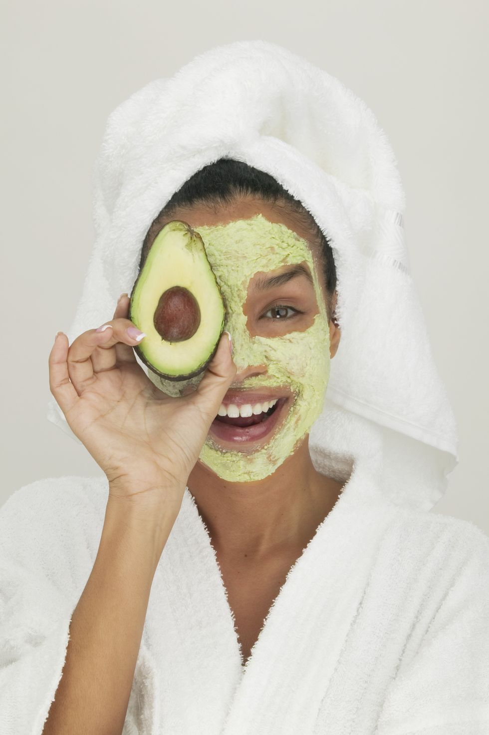 Portrait of a young woman wearing a facial mask holding a slice of avocado