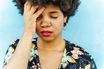 omicron, headaches, portrait of woman, hand on forehead, blue wall in the background