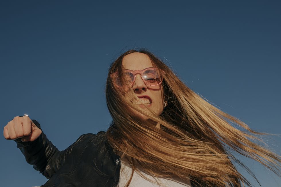 portrait of aggressive young woman punching under blue sky