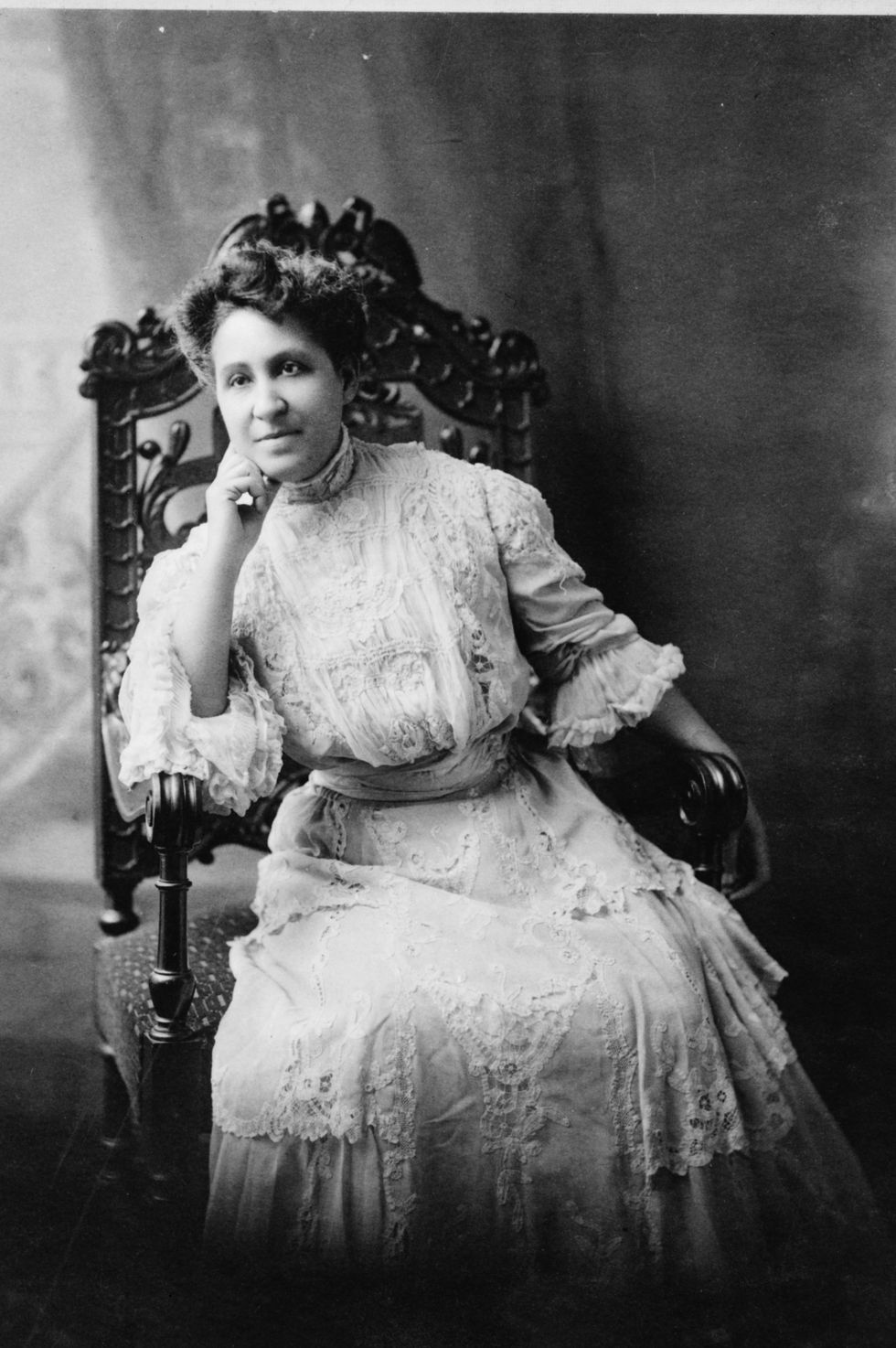 mary church terrell sits in a high backed chair in a lacy dress, she leans against on hand as her elbow rests on the armrest