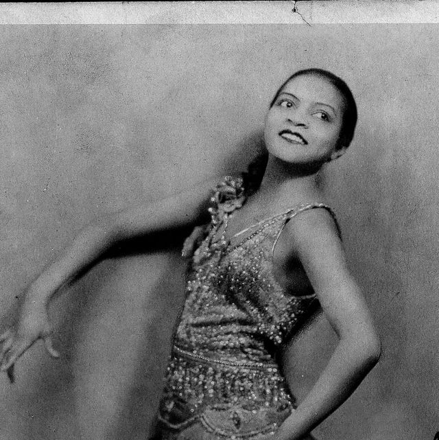 a woman poses with one hand on her hip and the other extended in front of her as she smiles and looks to the right