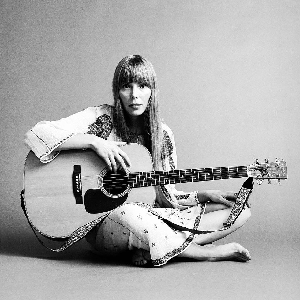 joni mitchell poses for a black and white photo while seated and holding a guitar on her lap