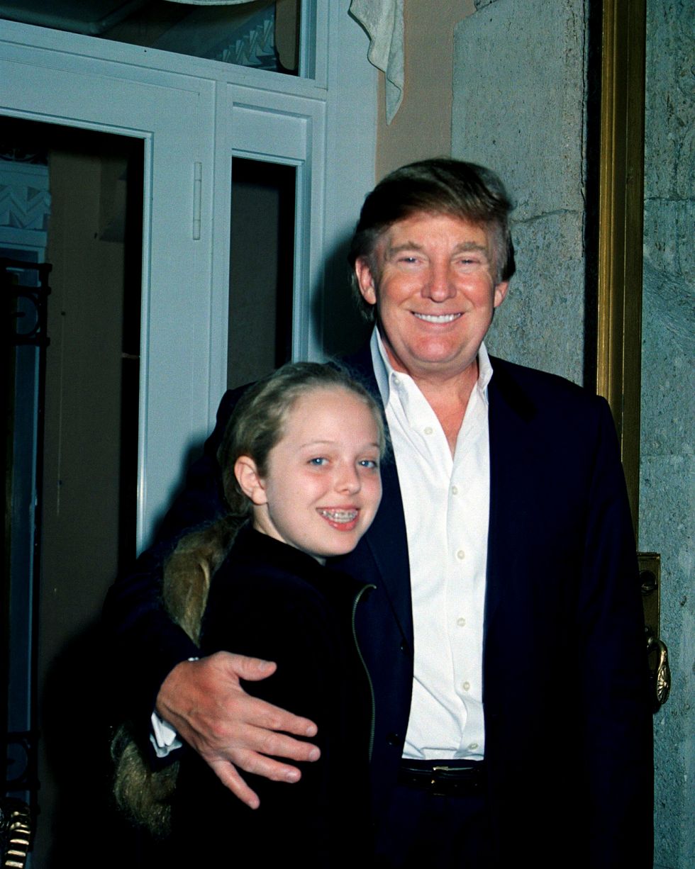 a girl and her father hug and smile at the camera while standing near a door