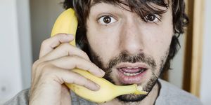 Portrait of astonished young man telephoning with banana