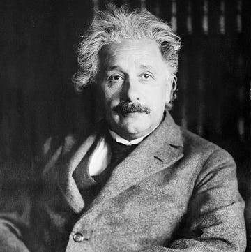 albert einstein sitting in front of a bookcase with his arms folded