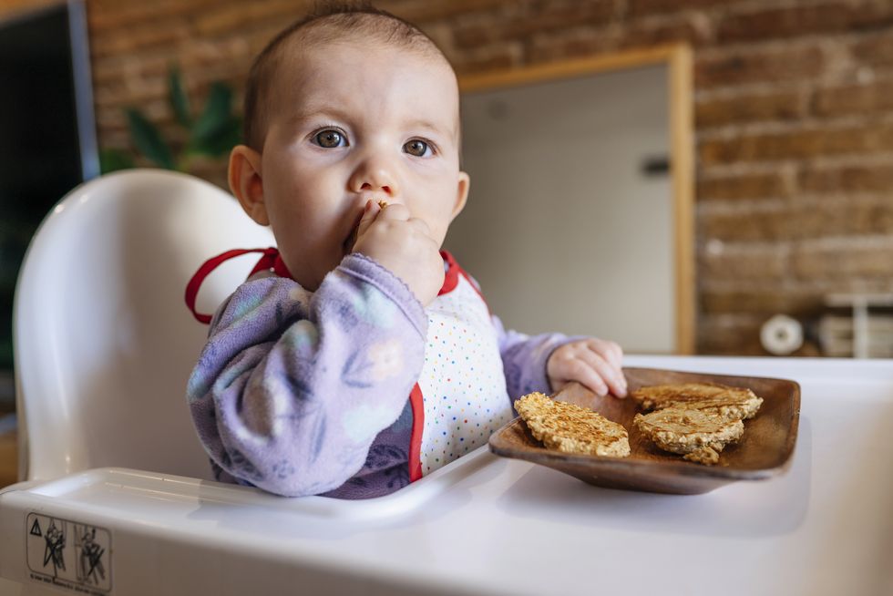 bebé comiendo en la trona con las manos tostadas de pan
