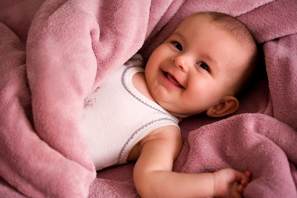 portrait of baby in a white tank style shirt smiling and wrapped in a soft pink blanket