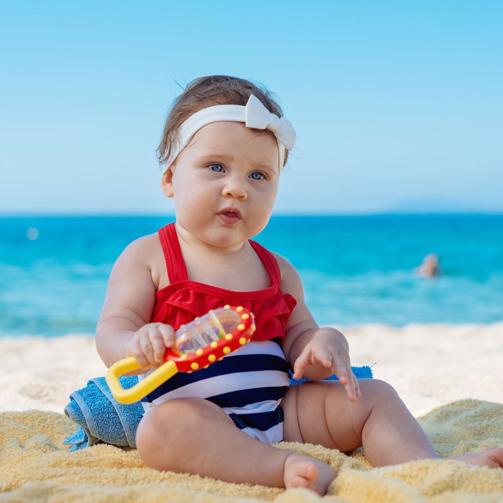 niña sentada en la arena de la playa con juguete