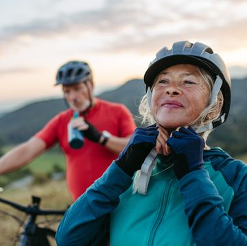 portrait of beautiful senior couple on bike ride in autumn nature taking break, drinking water from sport bottle and fastening helmet