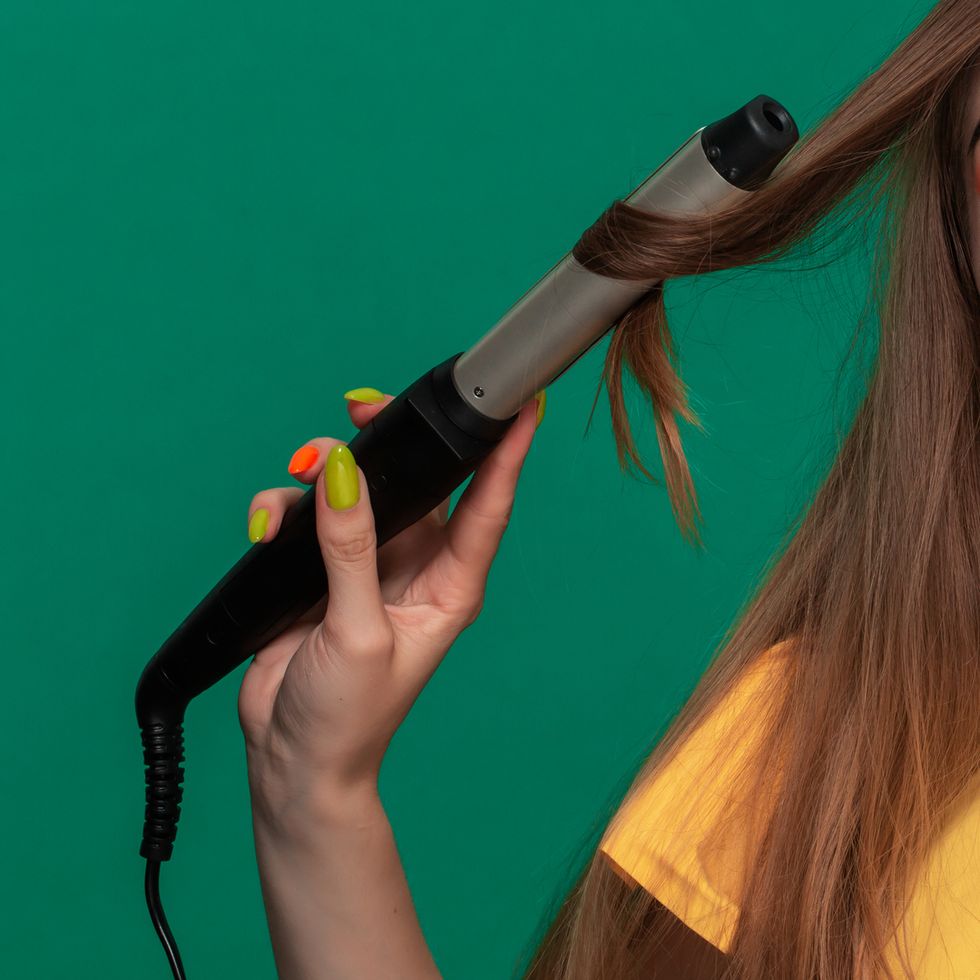 portrait of beautiful young woman with bright color make up having probems doing hair style herself with a curling iron