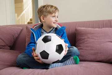 portrait of blond boy 6 7 sitting on sofa and holding soccer ball