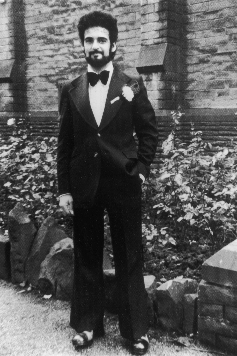 peter sutcliffe wearing a tuxedo and standing for a photo outside a stone building