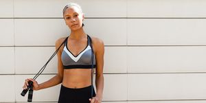 Portrait Of Confident Young Woman With Jump Rope Standing Against Wall