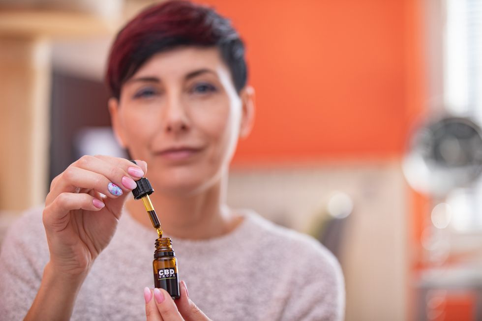portrait of content adult woman holding cbd oil drops in domestic room