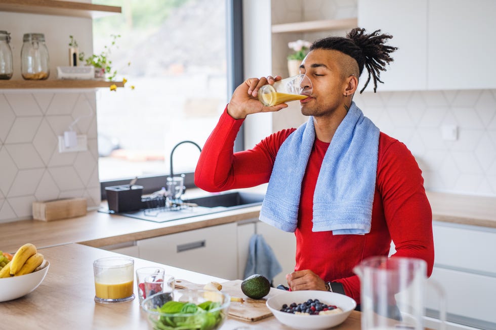 a portrait of fit mixed race man resting after doing exercise at home, drinking juice