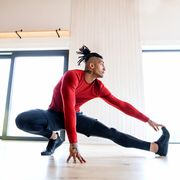 a portrait of fit mixed race man with dreadlocks doing exercise at home, stretching