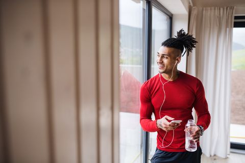 a portrait of fit mixed race man with smartphone and earphones at home, listening to music