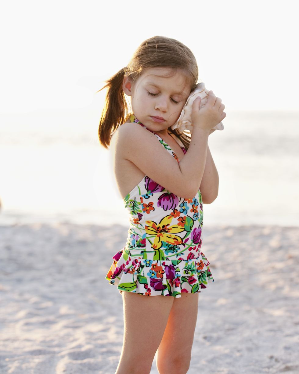 girl in floral print swimsuit listening to seashell at beach
