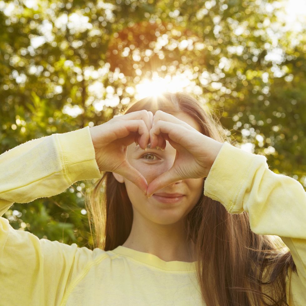 portrait of girl making heart shape with hands in park