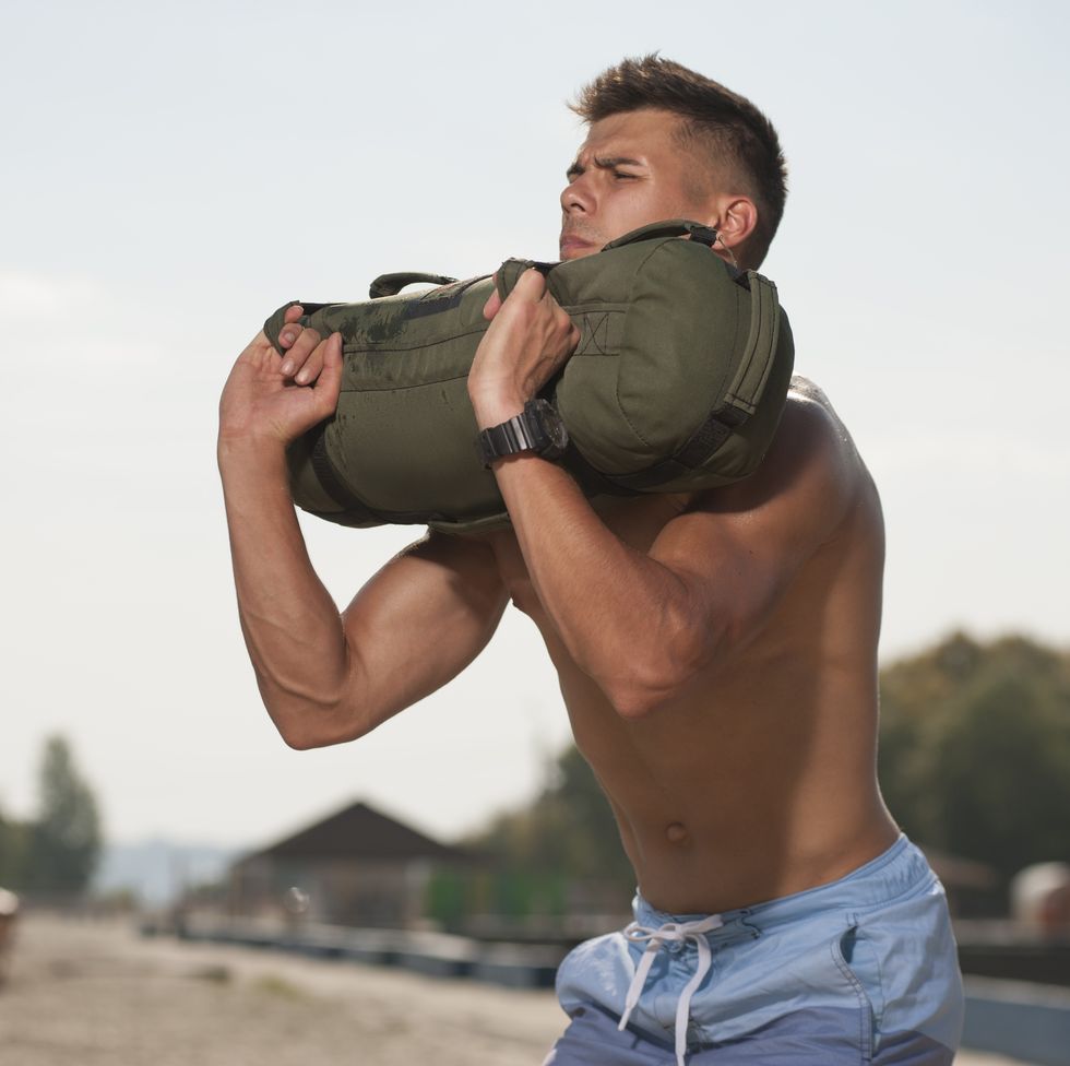 Portrait of handsome man training at the beach with sand bag equipment.