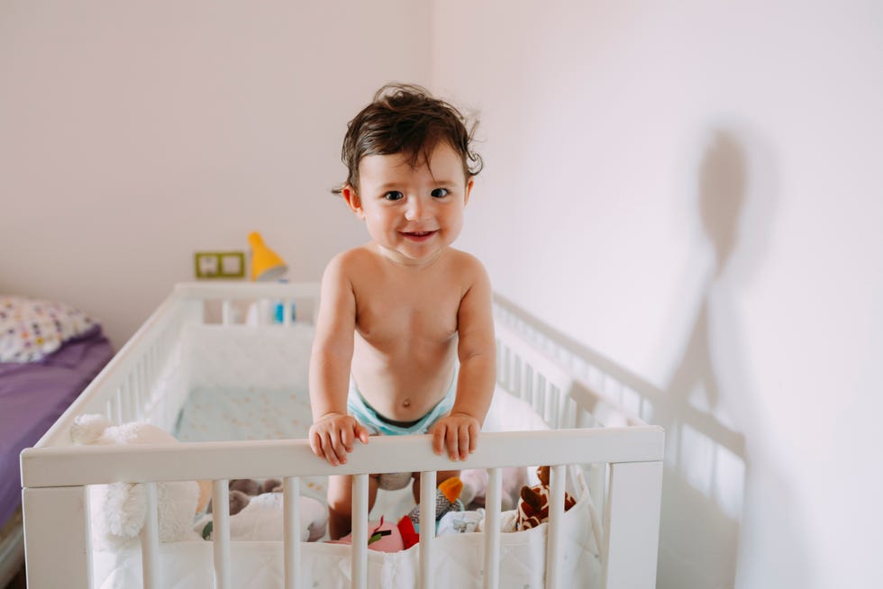 un bebé, sonriente y en pañal, juega con su cuna