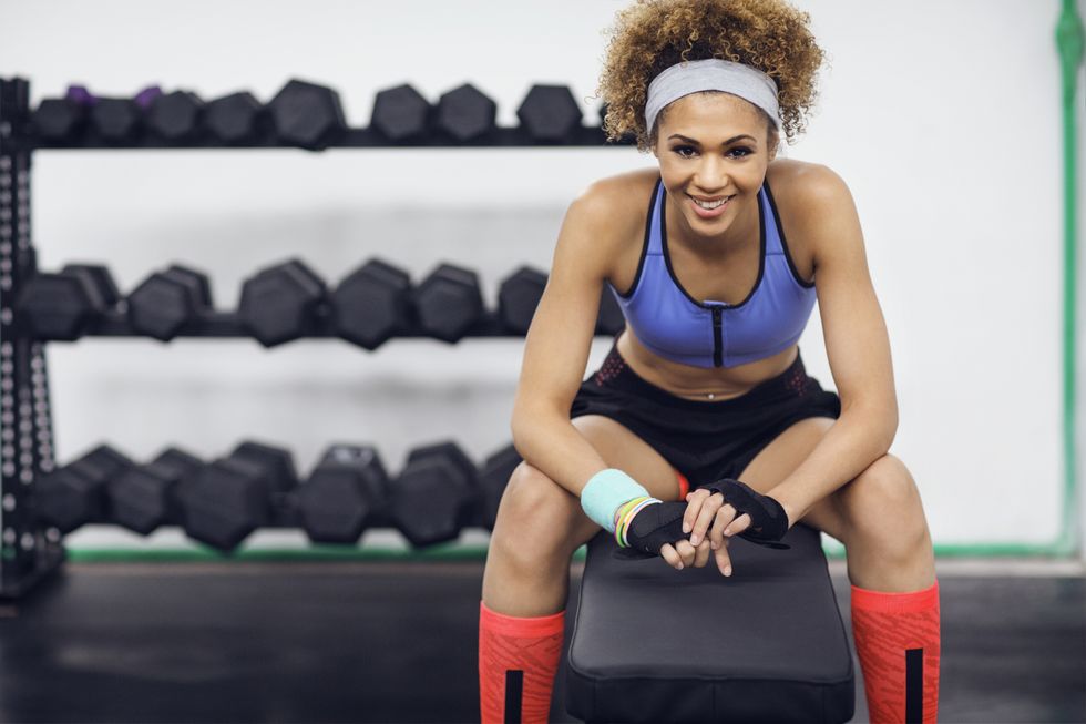 portrait of happy female athlete sitting on bench at gym