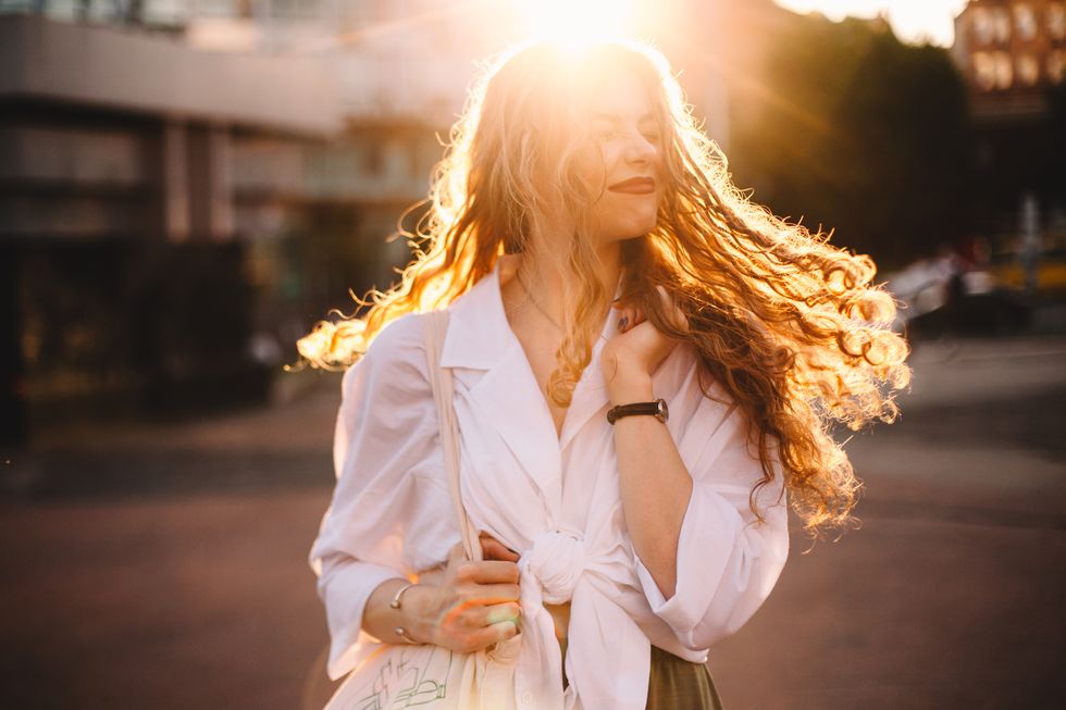 portrait of happy successful woman with tousled hair in city at sunset