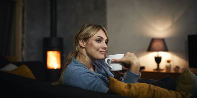 Portrait of happy woman with cup of tea relaxing on couch at home in the evening