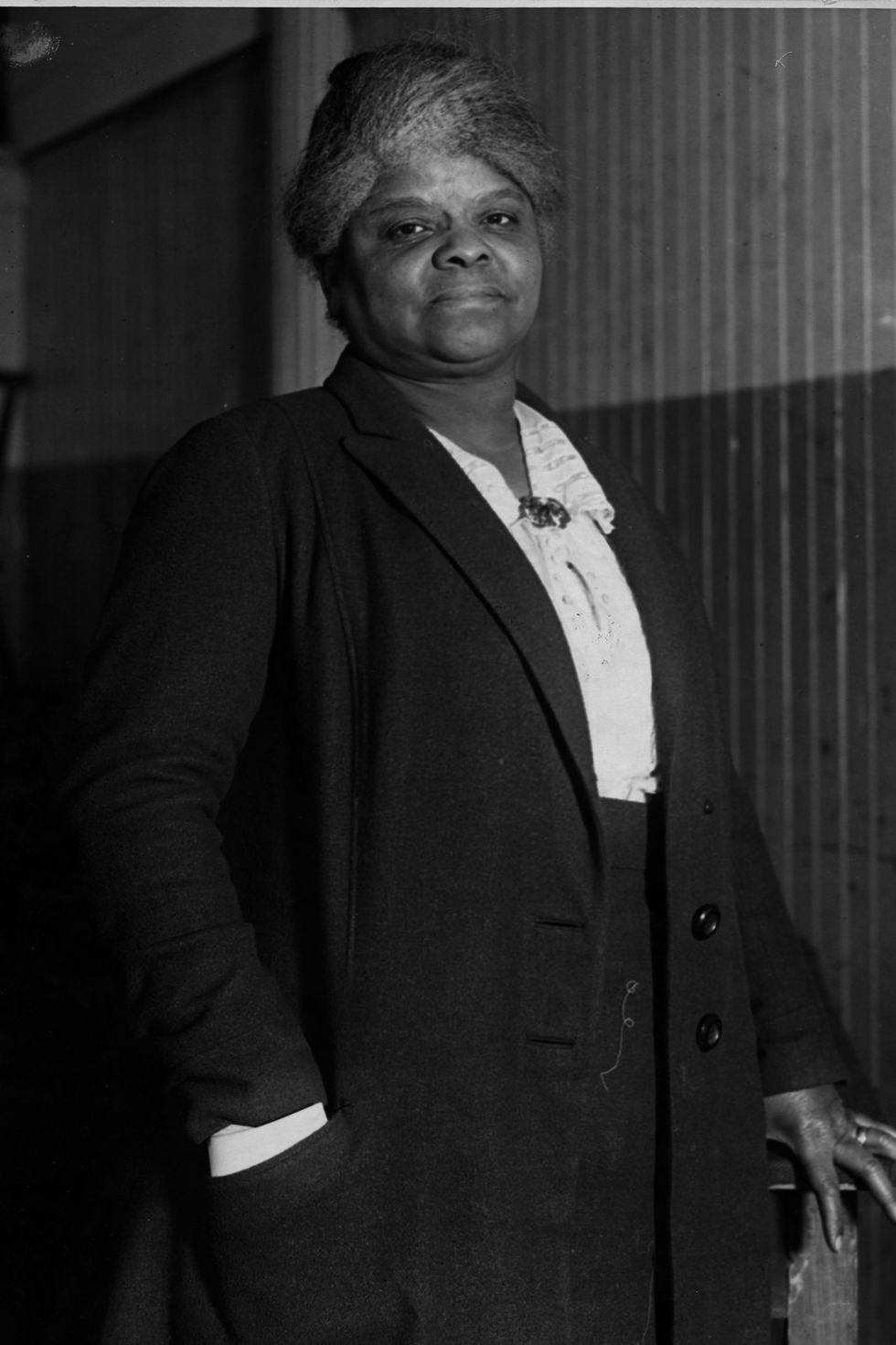ida b wells stands and looks at the camera, she wears a long jacket, light colored blouse and dark bottoms