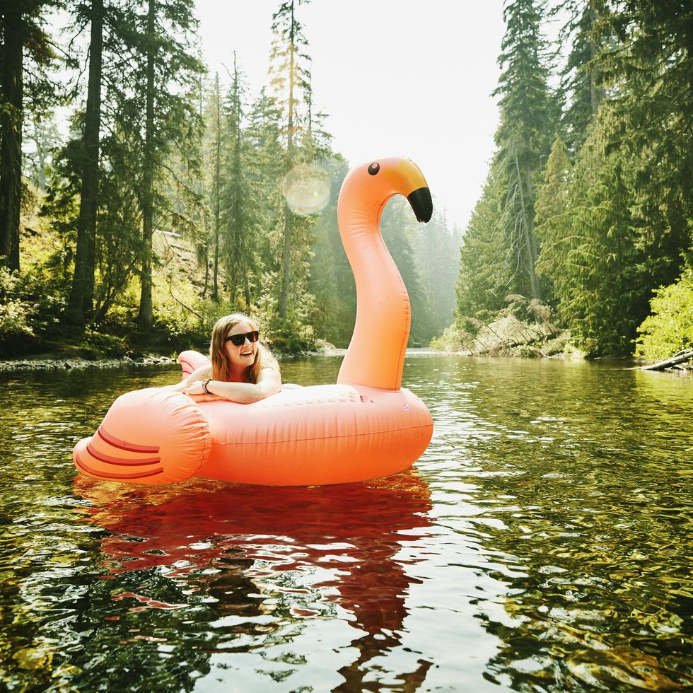 portrait of laughing woman floating down river  on inflatable pink flamingo as a fun camping activity