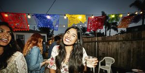 Portrait of laughing woman sharing drinks with friends in backyard on summer evening