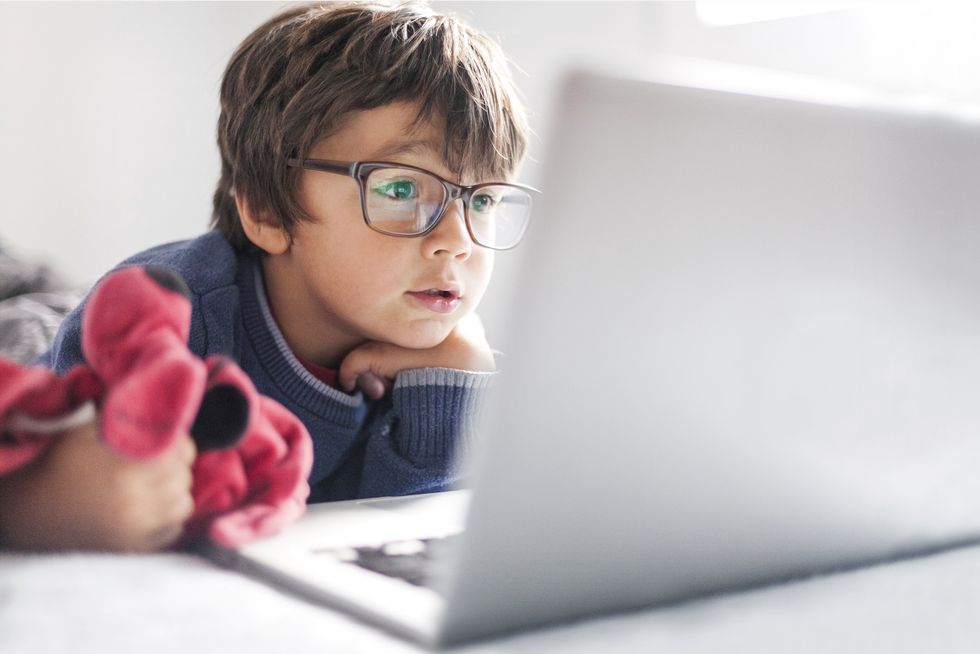 portrait of little boy wearing oversized glasses looking at laptop