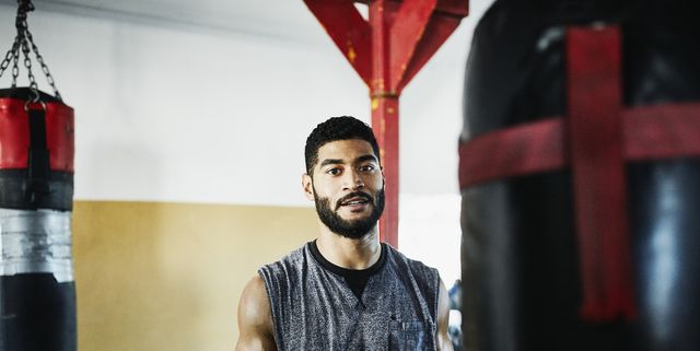 portrait of male boxer standing by heavy bag in boxing gym
