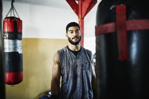 portrait of male boxer standing by heavy bag in boxing gym