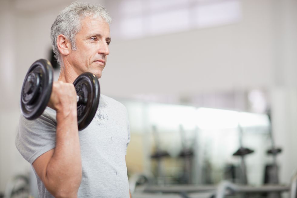 Portrait of man holding barbell in gymnasium