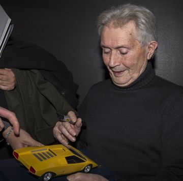 portrait of marcello gandini while he autographs a model car
