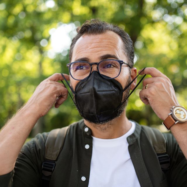 portrait of mature man walking and putting on face mask outdoors in park