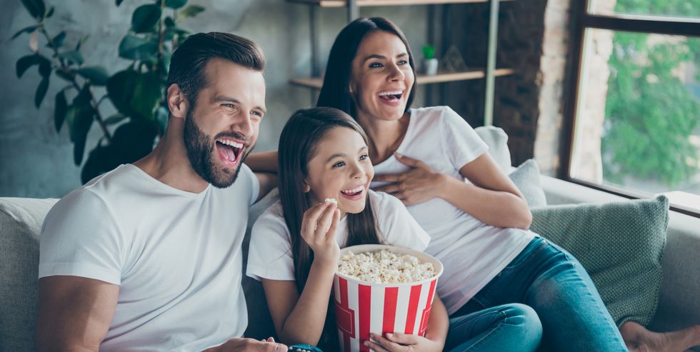 portrait of nice attractive lovely positive glad cheerful cheery family wearing casual white t shirts jeans denim sitting on sofa having fun watching funny video enjoying spending free time