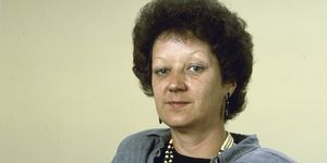 norma mccorvey, wearing a grey pantsuit, black shit, and beaded necklace, looking directly at the camera