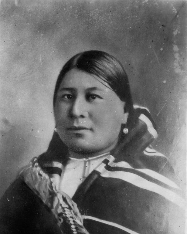 a black and white portrait of anna brown, wearing native american clothing and looking directly into the camera