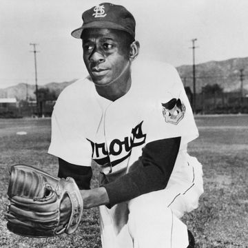 baseball pitcher leroy "satchel" paige kneels on a grass field and wears his st louis browns uniform, hat and baseball glove