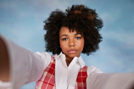 portrait of serious teenage girl with afro hairstyle taking selfie against colored background